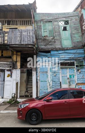 Auto rossa di fronte ad una casa completamente fatiscente dipinta in diversi colori pastello. Casco Viejo, Panama City, Panama Foto Stock