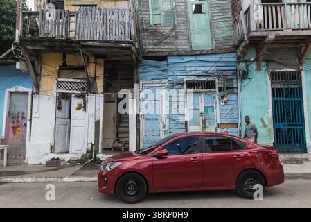 Auto rossa di fronte ad una casa completamente fatiscente dipinta in diversi colori pastello. Casco Viejo, Panama City, Panama Foto Stock
