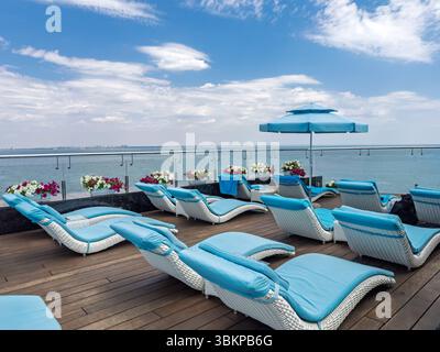 Idilliaco scenario delle vacanze estive. Sedie a sdraio vuote su un solarium che si affaccia sull'oceano calmo. Concetto di viaggio, fuga e vacanza serena. Foto Stock