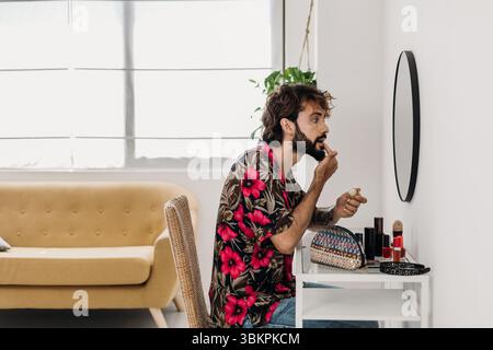 Giovane che applica il balsamo per le labbra seduto al suo tavolo da toeletta Foto Stock