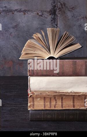 Un romanzo aperto giace su una pila di vecchi libri su sfondo marrone Foto Stock