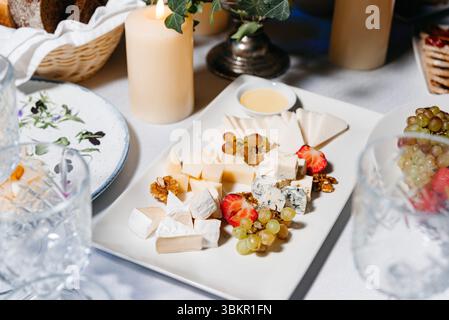 Elegante tagliere di formaggi servito con frutta assortita, noci e salsa subacquea, ideale per eventi di alto livello e riunioni formali. Foto Stock