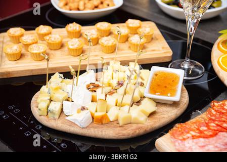 Vassoio di formaggi assortiti con cubetti di vari formaggi, noci e marmellata dolce serviti su un tavolo di legno per antipasti o abbinamenti di vini. Foto Stock