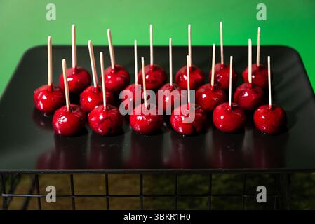 Mele di caramelle rosse brillanti disposte in file su un vassoio nero, ciascuna con un bastoncino di legno, perfette per eventi festivi o dessert. Foto Stock