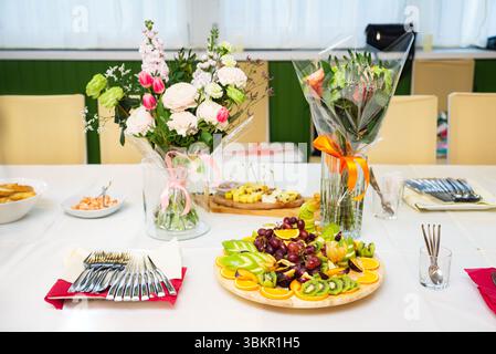 Tavolo da festa splendidamente allestito con frutta fresca tagliata, mazzi di fiori, utensili e spuntini leggeri per una festa o un evento. Foto Stock