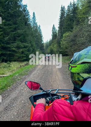 Persona in sella a un ATV attraverso una strada sterrata circondata da una fitta pineta, indossa casco e attrezzatura, catturando l'emozione dell'esplorazione fuoristrada in n Foto Stock