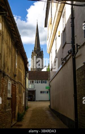 Una vista suggestiva lungo una stretta strada a Saffron Walden, in Inghilterra, con una guglia della chiesa che domina lo sfondo. Foto Stock