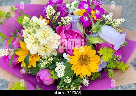 Bouquet di fiori avvolti di fiori primaverili misti. Splendidi fiori freschi dai colori vivaci. Bouquet di compleanno con peonie e girasoli Foto Stock
