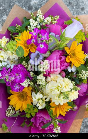 Bouquet di fiori avvolti di fiori primaverili misti. Splendidi fiori freschi dai colori vivaci. Bouquet di compleanno con peonie e girasoli Foto Stock