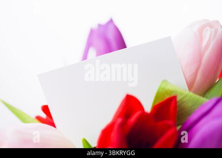 La carta bianca bianca galleggia tra un bouquet di tulipani multicolori in un design piatto e uno spazio per le copie Foto Stock