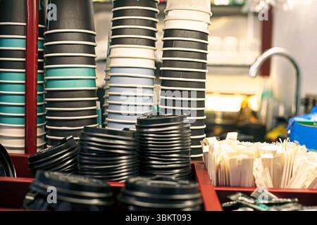 tazze per bevande monouso impilate in colonne con sacchetti di zucchero e cannucce in un caffè Foto Stock