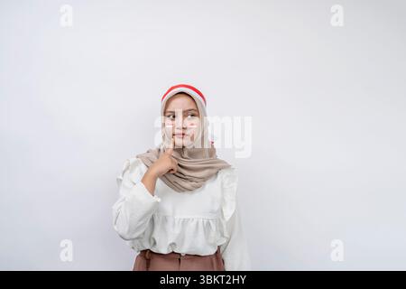Ritratto di bella giovane donna musulmana asiatica celebrare il giorno dell'indipendenza indonesiana cercando seriamente di pensare alla domanda e guardando lo spazio di copia Foto Stock