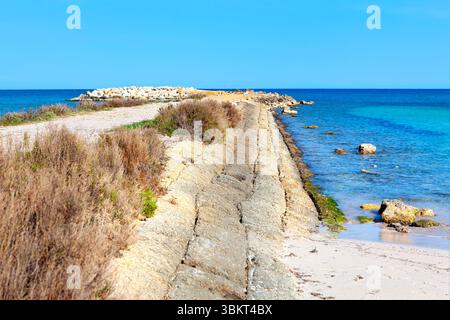 Il sentiero costiero si snoda lungo una diga di pietra, che conduce alle tranquille acque turchesi. Sentiero fiancheggiato da una diga di pietra che conduce a un tranquillo Foto Stock