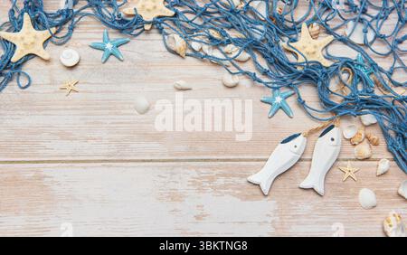 Pesci decorativi in legno, conchiglie, stelle marine e reti da pesca sono disposti su uno sfondo rustico di legno imbiancato, creando un perfetto tema nautico Foto Stock