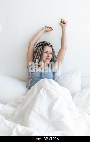 Giovane donna felice che si allunga nel letto bianco. Foto Stock