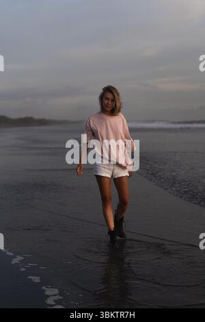 Giovane donna informale passeggiando lungo la spiaggia di Bali all'ora d'oro Foto Stock
