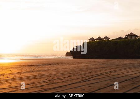 Tramonto dorato su una spiaggia tranquilla con tetti balinesi tradizionali Foto Stock