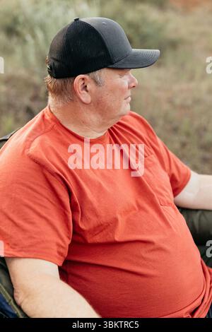 Uomo di mezza età in cap che si rilassa all'aperto nel campeggio forestale Foto Stock