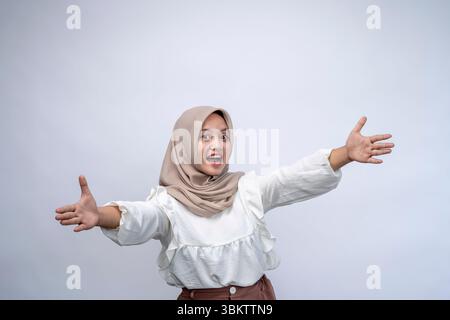 Mi dia Hug. Ritratto della giovane donna indonesiana positiva che indossa hijab che si allunga le mani a camera, felice sorridente Millennial apertura braccia per Em Foto Stock
