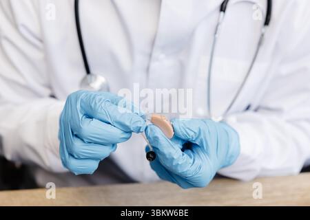 Un otolaringologo tiene in mano un apparecchio acustico. Il medico consulta il paziente. Foto Stock