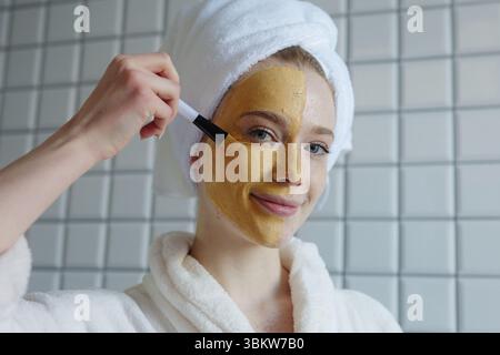 Una donna sta applicando una maschera viso ringiovanente mentre si gode un'atmosfera rilassante in un ambiente spa Foto Stock