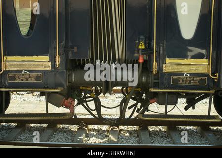 Sistema di accoppiamento meccanico che collega due carrelli Venice Simplon-Orient-Express blu e oro su un binario ferroviario, con tamponi visibili, tubi flessibili, alimentazione CA Foto Stock