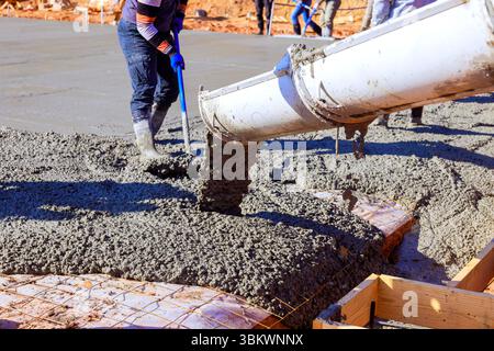 Gli operai edili versano calcestruzzo fresco sulle lastre preparate, garantendo solide fondamenta. Foto Stock