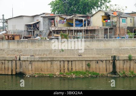 Le case improvvisate fiancheggiano una sponda fluviale inquinata, un insediamento urbano informale che si trova ad affrontare sfide ambientali. Foto Stock