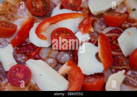 Delizioso primo piano di una pizza italiana appena sfornata condita con pomodori ciliegini maturi, cremose fette di mozzarella, vivaci strisce di pepe rosso e s Foto Stock