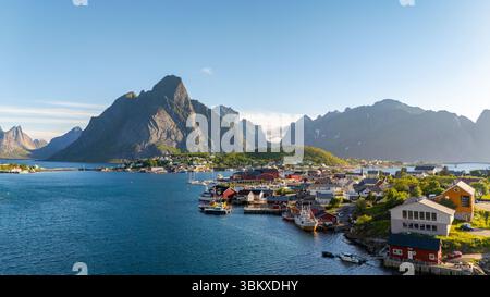 Annidato tra vette spettacolari e acque tranquille, questo villaggio costiero di Reine a Lofoten in Norvegia mette in mostra case colorate e barche vivaci sotto un cielo azzurro. Una destinazione perfetta per una vacanza. Foto Stock