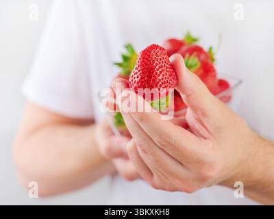 Fragole fresche in piatto in mani maschili per il trattamento o lo spettacolo. Il giovane uomo in maglietta bianca tiene la fragola in mano per un regalo. Elemento per la progettazione Foto Stock