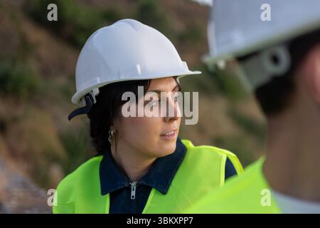 Ingegnere donna che indossa un elmetto per discutere del progetto con un collega Foto Stock