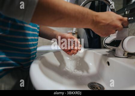 Persona che lava le mani sotto l'acqua corrente in un lavandino in ambiente domestico Foto Stock