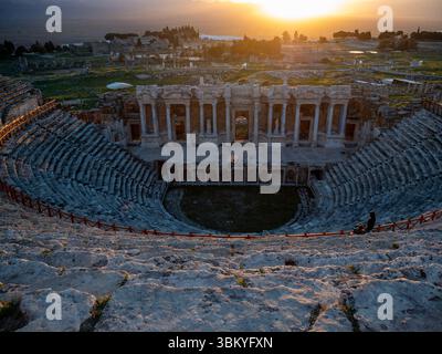 Due persone sono in piedi sui gradini dell'antico teatro di Hierapolis, Turchia, ammirando la vista delle rovine e del tramonto. Foto Stock