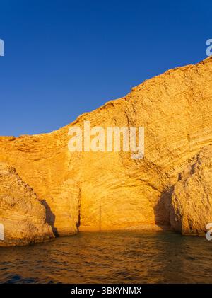 Splendide scogliere calcaree dorate che torreggiano su tranquille acque blu, illuminate dalla calda luce del tramonto. Isole Koufonisia, Cicladi, Grecia Foto Stock