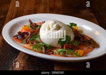 Insalata di pomodoro ravvicinata con burrata fresca su un piatto bianco su un tavolo di legno Foto Stock