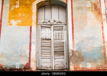 Cuba, l'Avana. Edificio in stucco e legno, con persiane e porte con feritoie. Blu e giallo, vernice sbucciante. Foto Stock