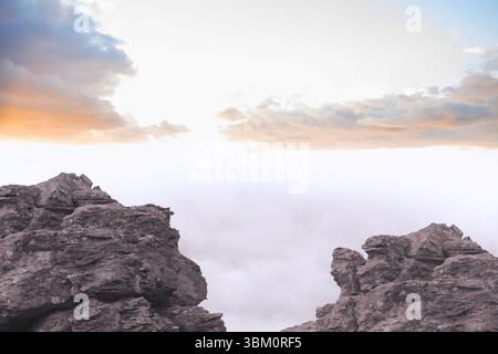 Un paio di formazioni rocciose robuste mostrano un abisso pieno di nuvole all'alba in un design piatto Foto Stock