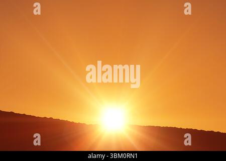 Sfera solare luminosa che risplende sul cielo arancione sulla silhouette di una collina in un design piatto, con raggi stellati Foto Stock