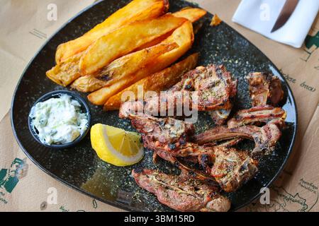 Un tradizionale pasto greco con agnello alla griglia, patatine fritte croccanti e cremosa tzatziki. Un gustoso assaggio di Creta servito fresco in una taverna locale. Foto Stock