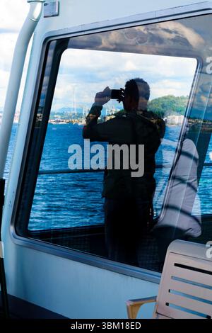 Silhouette dell'uomo che scatta foto sul traghetto Bainbridge Ferry avvicinandosi allo skyline di Seattle, nello stato di Washington, Stati Uniti. Foto Stock