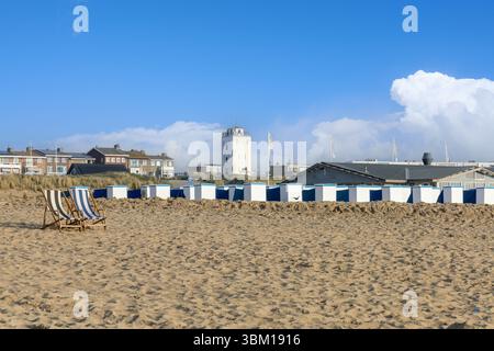 Sdraio su una vasta spiaggia di sabbia a Katwijk aan Zee, con file di cabine bianche e blu e un faro lontano sotto un cielo limpido, evocano un pe Foto Stock