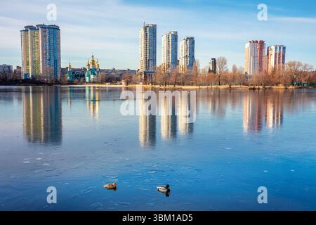 Skyline, città di Kiev al mattino. Riva sinistra del fiume Dnieper. Lakeshore con alberi la mattina. Splendido riflesso degli edifici nel lago Foto Stock
