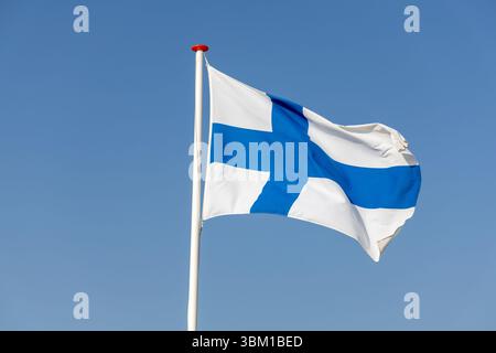 Bandiera finlandese che sventola nel vento contro un cielo azzurro. Un simbolo dell’orgoglio e dell’identità nazionale della Finlandia, catturato in una giornata di sole brillante. Foto Stock