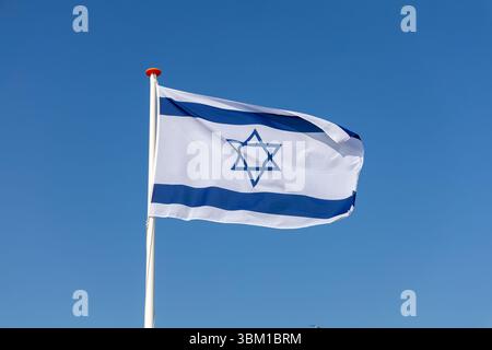 La bandiera nazionale di Israele, con la Stella di Davide e le strisce blu, ondeggia orgogliosamente contro un cielo azzurro limpido, a simboleggiare l'identità nazionale. Foto Stock