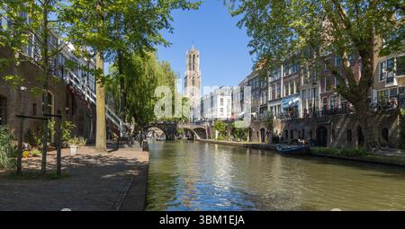 Una vista pittoresca del canale Oudegracht a Utrecht, Paesi Bassi, con la Torre del Duomo che si erge sopra gli edifici storici sotto un cielo azzurro. UTR Foto Stock