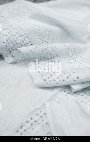 Uno scatto ravvicinato rivela gli intricati dettagli del tessuto bianco in pizzo con occhiello. Il tessuto è leggermente drappeggiato e sfoggia la sua delicata traforatura a motivi geometrici Foto Stock