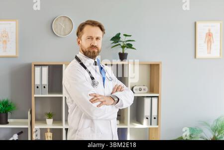 Medico professionista sicuro di sé in camice bianco in piedi braccia incrociate in armadietto, che lavora in clinica Foto Stock