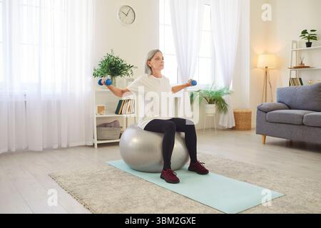 Esercizio di palla di stabilità per equilibrio, manubrio, fitness, donna sportiva anziana, vecchio yoga a casa Foto Stock