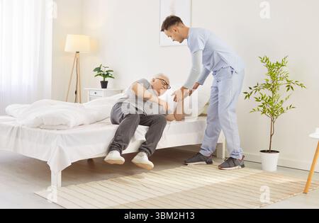 Medico o operatore sanitario che assiste l'uomo anziano a stare in mattinata presso la casa di cura Foto Stock